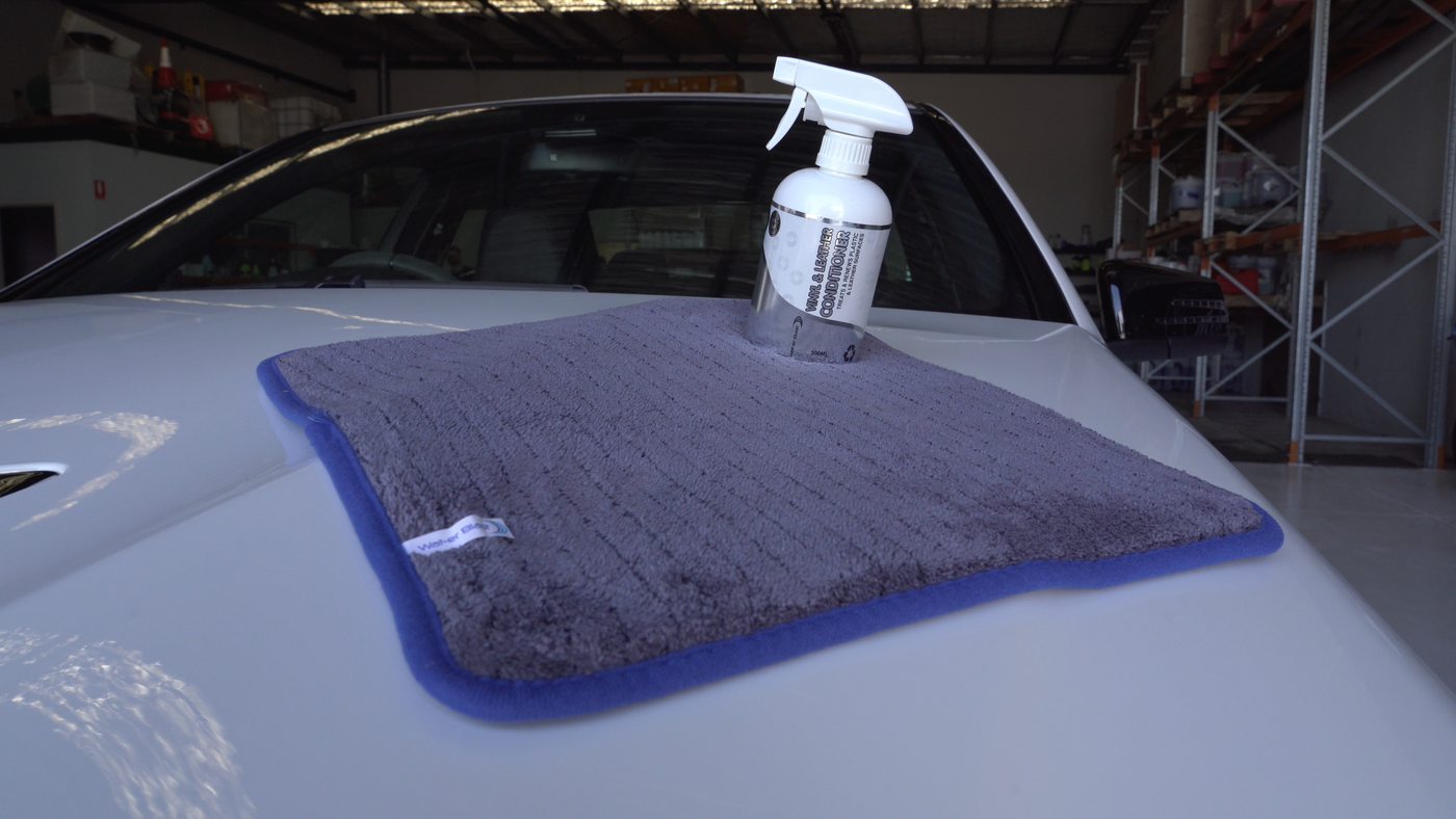 Spray Bottle of 500ml Interior Care Care Product "Vinyl and Leather Conditioner" on a Large Microfibre Drying Towel on top of a White Car